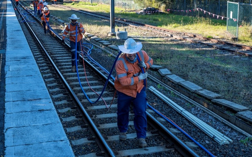 workers carrying cables along rail line.