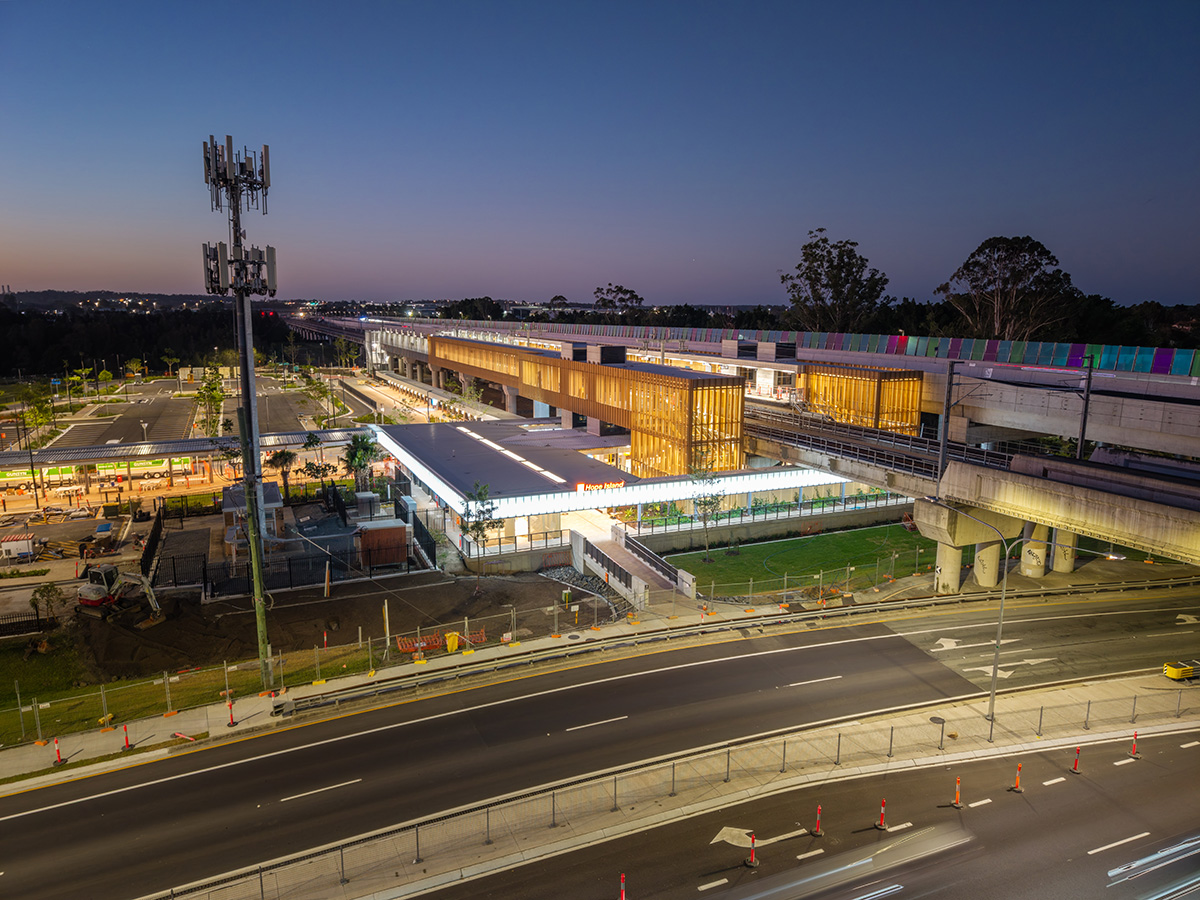 Night view of Hope Island station with illuminated concourse, platforms, and road below.