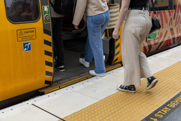 People walking on to a QR train with new accessibility rubber fingers between the train and the platform.